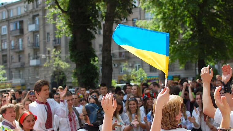 A crowd in embroidered vyshyvanky raising the flag of Ukraine on a summer street